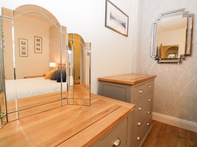 A bedroom dresser with a three-panel mirror and a chest of drawers with framed pictures on the wall at Tethera in Bowness-On-Windermere