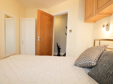 A bedroom with a bed and pillows a wooden door a white wardrobe a wall mirror and wall cabinets at Tethera in Bowness-On-Windermere