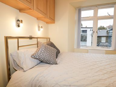 A bedroom with a bed pillows wall lights and a large window at Tethera in Bowness-On-Windermere