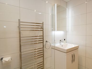 A bathroom with a sink cabinet a wall-mounted mirror a towel rack and a toilet paper holder at Tethera in Bowness-On-Windermere