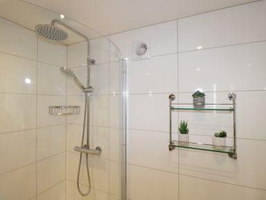 A shower area with a rain shower head hand shower white tiled walls and a glass shelf with small potted plants at Tethera in Bowness-On-Windermere