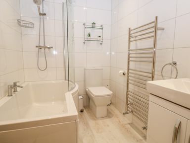A bathroom with a bathtub shower combination toilet towel warmer and sink with cabinet at Tethera in Bowness-On-Windermere
