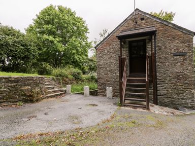 Stone building with wooden stairs and door next to stone steps and trees at Ribby Barn in Lerryn