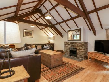 A living room with a wooden beams ceiling a stone fireplace a wooden coffee table two leather sofas a floor lamp and a television at Ribby Barn in Lerryn
