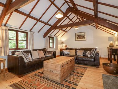 A living room with two leather sofas a wooden chest coffee table exposed wooden beams and patterned rugs at Ribby Barn in Lerryn