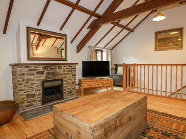 A living room with a stone fireplace wooden beams a television on a wooden table and a wooden chest at Ribby Barn in Lerryn