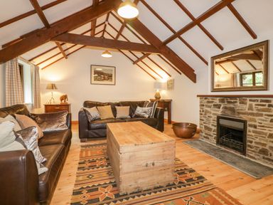 A living room with leather sofas a wooden coffee table a stone fireplace and exposed ceiling beams at Ribby Barn in Lerryn