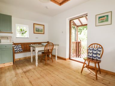 A kitchen area with wooden floor a table chairs a bench and pictures on the wall at Ribby Barn in Lerryn