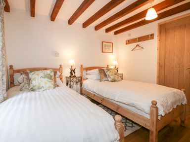 A bedroom with two wooden single beds with white bedding and floral pillows at Ribby Barn in Lerryn