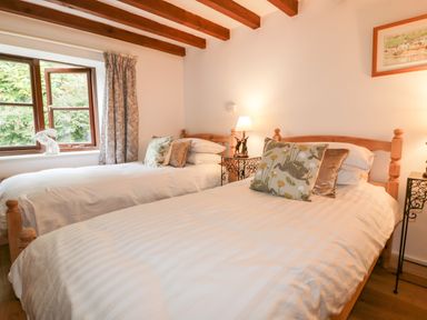 A bedroom with two single beds wooden frames pillows bedside tables lamps and a window at Ribby Barn in Lerryn