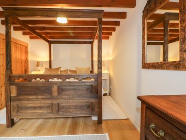 A bedroom with a wooden four-poster bed bedside tables with lamps a wooden dresser and a large mirror at Ribby Barn in Lerryn