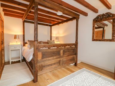 A bedroom with a wooden four-poster bed two bedside tables with lamps a wooden floor and a carved wooden mirror on the wall at Ribby Barn in Lerryn