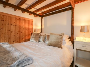 A bedroom with a four-poster bed pillows bedside tables with lamps and a wooden wall at Ribby Barn in Lerryn