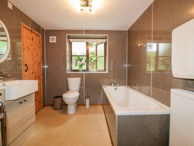 A bathroom with a bathtub toilet sink wooden door and a window with flowers at Ribby Barn in Lerryn