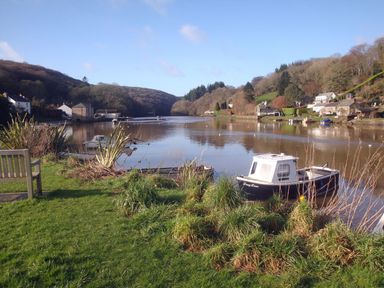 A river with boats docked near grassy riverbanks and houses on the hills at Ribby Barn in Lerryn