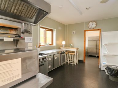 A commercial kitchen with stainless steel appliances stools and a window at Llety Ceiro in Bow Street Wales