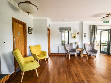 A sitting area with yellow and gray chairs wooden floors and a wooden door at Llety Ceiro in Bow Street Wales