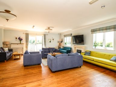 A living room with multiple sofas a wall-mounted television and windows with plaid curtains at Llety Ceiro in Bow Street Wales
