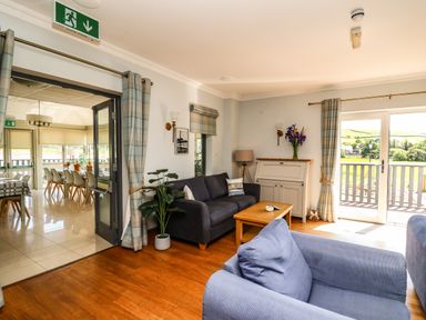 A sitting room with couches a coffee table and a cabinet with flowers near glass doors opening to a balcony at Llety Ceiro in Bow Street Wales