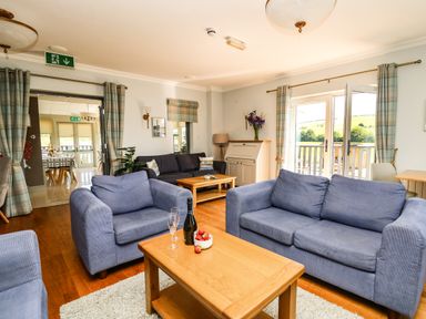 A living room with blue sofas wooden tables and glass doors opening to a balcony at Llety Ceiro in Bow Street Wales