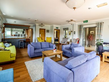 A lounge area with blue and green sofas a wooden coffee table a bar and various chairs at Llety Ceiro in Bow Street Wales