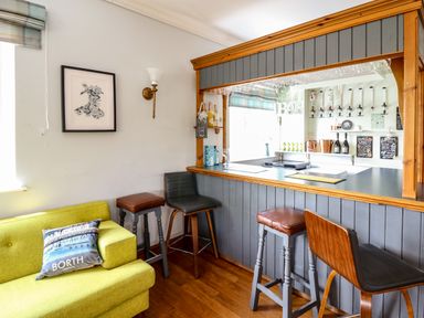 A home bar area with stools a green sofa with a pillow and framed picture on the wall at Llety Ceiro in Bow Street Wales