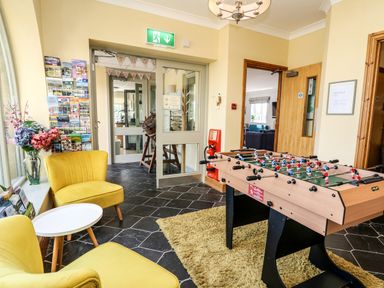 A lounge area with yellow chairs a foosball table and brochures on display at Llety Ceiro Bow Street Wales