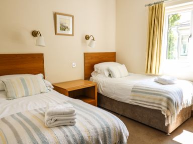 A bedroom with two single beds a wooden nightstand and a window with yellow curtains at Llety Ceiro in Bow Street Wales