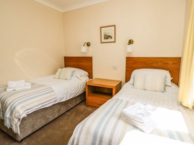 A bedroom with two single beds a wooden nightstand and wall lamps at Llety Ceiro in Bow Street Wales