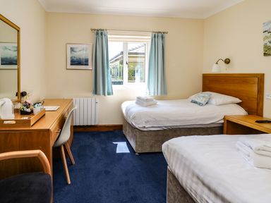 A bedroom with two single beds a desk with a chair and a window with curtains at Llety Ceiro in Bow Street Wales