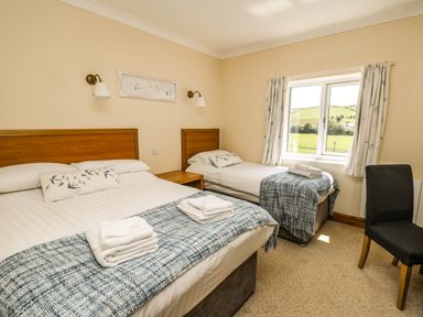 A bedroom with a double bed and a single bed with blankets and towels near a window with curtains and a chair at Llety Ceiro in Bow Street Wales