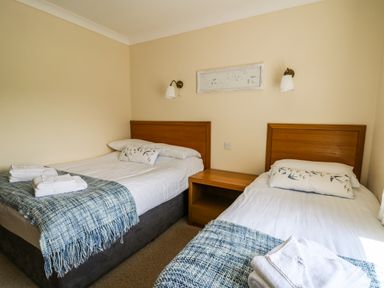A bedroom with two single beds with wooden headboards blue blankets and white towels at Llety Ceiro in Bow Street Wales