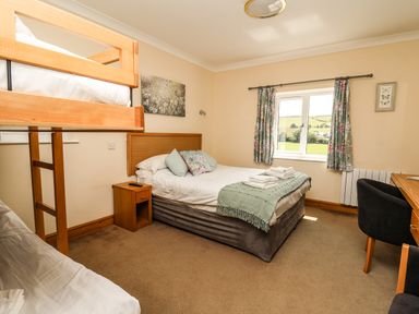 A bedroom with a double bed and bunk beds a desk and chair and a window with floral curtains at Llety Ceiro in Bow Street Wales
