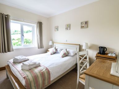 A bedroom with a double bed two bedside tables two lamps a window curtains a desk a chair and a tray with a kettle and cups at Llety Ceiro in Bow Street Wales