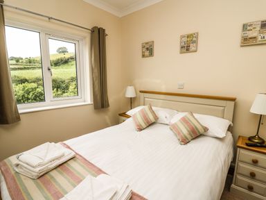 A bedroom with a double bed two bedside tables lamps a window and folded towels at Llety Ceiro in Bow Street Wales