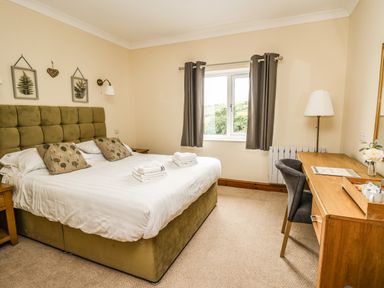 A bedroom with a double bed two nightstands a window with curtains and a wooden desk with a chair at Llety Ceiro in Bow Street Wales