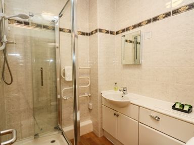 A bathroom with a glass shower enclosure a sink with a mirror above and cabinets below at Llety Ceiro in Bow Street Wales