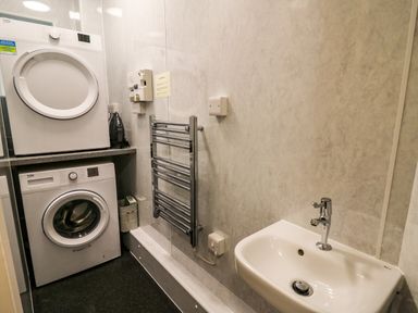 A laundry room with a washing machine, dryer, sink, and a chrome towel rack at Llety Ceiro in Bow Street Wales