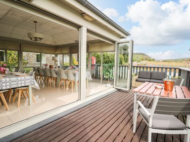 A dining area with tables and chairs inside next to a wooden deck with outdoor seating at Llety Ceiro in Bow Street Wales