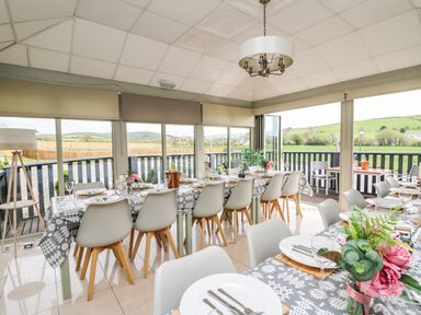 A dining area with long tables and white chairs set with plates and cutlery at Llety Ceiro in Bow Street Wales