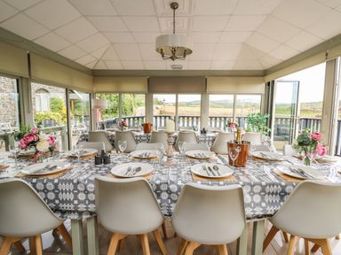 A dining room with long tables set for a meal and overlooking countryside at Llety Ceiro in Bow Street Wales