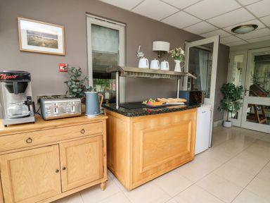 A food counter with fruit and bread next to a wooden cabinet with coffee machine toaster and kettle in a room at Llety Ceiro Bow Street Wales