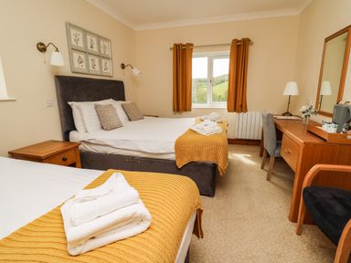 A bedroom with two beds yellow blankets and a wooden desk at Llety Ceiro in Bow Street Wales
