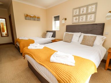 A bedroom with a double bed and a single bed each with yellow blankets and white towels at Llety Ceiro in Bow Street Wales