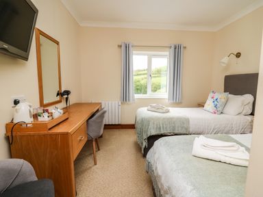 A bedroom with two single beds a desk with a chair a wall-mounted television and a window with curtains at Llety Ceiro in Bow Street Wales