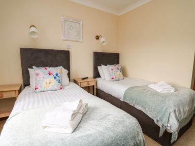 A bedroom with two single beds each with a floral pillow and folded towels on the bed at Llety Ceiro in Bow Street Wales