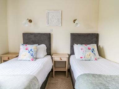 A bedroom with two single beds with floral pillows and a nightstand between them at Llety Ceiro in Bow Street Wales