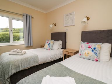 A bedroom with two single beds with floral pillows and towels on blankets at Llety Ceiro in Bow Street Wales