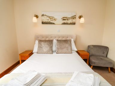 A bedroom with a bed pillows bedside tables wall lights and an armchair at Llety Ceiro Bow Street Wales
