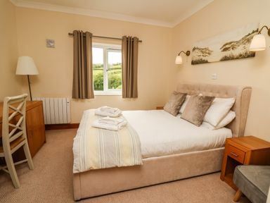 A bedroom with a double bed a desk chair and window with curtains at Llety Ceiro in Bow Street Wales
